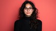 © Suphot - A young woman with curly hair and glasses poses confidently against a vibrant red background, embodying style and intelligence.