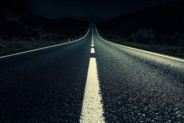 Canvas Print - A stark white road line cutting through a dark asphalt highway at night. 