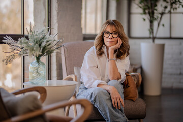 Wall Mural - Blond haired woman relaxing in an armchair by the window