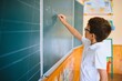 © Serhii - Cute little schoolboy diligent write chalk solve math problem dressed stylish uniform classroom blackboard background