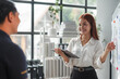 © amnaj - Young manager woman is holding a digital tablet and presenting a business plan on a whiteboard to her colleague