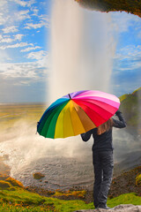 Wall Mural - A woman with a colorful umbrella poses in front of a waterfall - Amazing Seljalandsfoss waterfall in Iceland