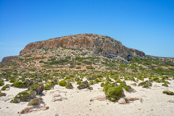 Scenic coast of Mediterranean Sea with sand and rocks - Crete, Greece, Balos Beach. Mountain landscape and green maquis plants. Beautiful, blue, clear sky