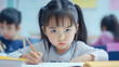 © Stefan - Portrait of a little Asian girl, a cute female student or toddler, with a frowning, unsatisfied, or nervous facial expression, writing with a pencil on paper in a classroom. Education and lesson.