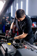 © Guys Who Shoot - in a car service a master in a black T-shirt uses a drill to unscrew the bolts in the engine part of the car replacing spare parts