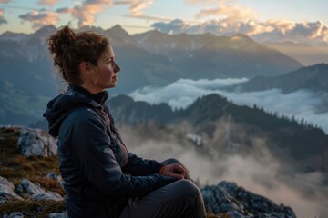 Wall Mural - A person sitting on the edge of a mountain, looking out over a valley and clouds.