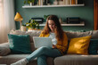 © Instacraft.Studio - A young woman sits on a couch in her living room, working on her laptop. The image conveys a sense of comfort, relaxation, and focus.