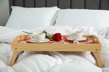 Wall Mural - Wooden tray with burning candles, rose, cups of drink and red paper hearts on bed indoors