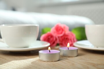 Poster - Burning candles, rose flowers and cups of drink on wooden table indoors