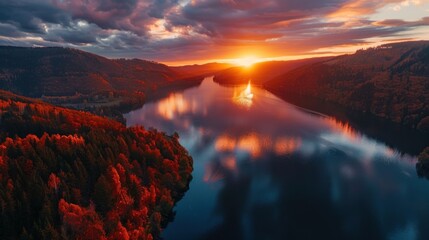 Wall Mural - Panoramic aerial landscape on sunset over majestic lake in mountains with autumn colored forest around. Clouds in sky and trees reflect in water in lake