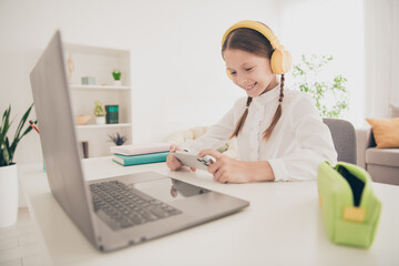 Poster - Photo of cute small girl study online laptop play game smart phone desk modern apartment indoors