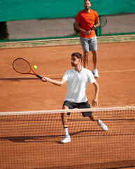 Competitive moment on court. Two men, professional tennis players in same team focusing on game, dynamically playing on clay court. Concept of sport, competition, active and healthy lifestyle