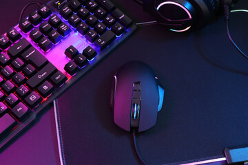 Wall Mural - Computer mouse, headset and RGB keyboard in neon lights on dark background, above view