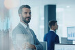 © Anna - Confident businessman in a modern office with financial graphs overlay. Represents leadership, finance, and professional success in a corporate environment.