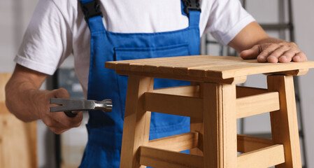 Wall Mural - Man repairing wooden stool with hammer indoors, closeup