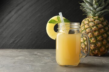 Wall Mural - Tasty pineapple juice in mason jar, mint and slice of fruit on grey textured table, closeup. Space for text