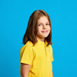 © master1305 - Side view portrait of beautiful teen girl wearing yellow polo shirt, posing with little tender smile on blue studio background. Happy confident child. Concept of childhood, kids emotions, lifestyle