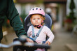 © Irina Schmidt - A smiling toddler girl wearing a pink helmet sits securely in a bicycle child seat, ready for a ride. The background is blurred, focusing on the child joyful expression