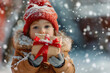 © Alberto Gonzalez  - A toddler in a red beanie and winter coat holding a gift, snowflakes falling around.