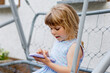 © Irina Schmidt - Cute little toddler girl playing with smartphone Healthy baby touching mobile phone with fingers, looking cartoons and having fun with educational apps. Child in garden outdoors