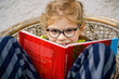 © Irina Schmidt - Little girl with eyeglasses reading book. Happy interested child learning.