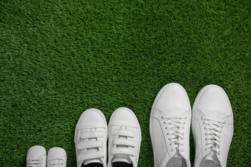 Wall Mural - Big and small shoes on green grass, top view. Space for text