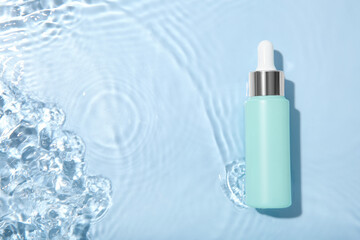 Wall Mural - Bottle of cosmetic product in water on light blue background, top view. Space for text