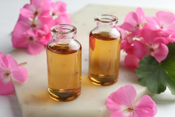 Wall Mural - Bottles of geranium essential oil and beautiful flowers on white table, closeup