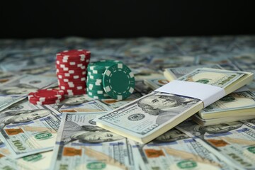 Many dollar banknotes and casino chips on black background, closeup