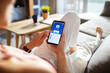 © Marko Geber - Close up of woman using bank app on smartphone from home sofa
