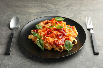 Delicious pasta with tomato sauce and basil served on grey textured table, closeup