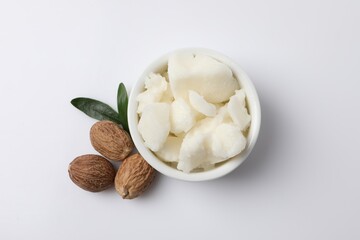 Shea butter in bowl and nuts on white background, flat lay