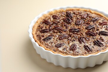 Delicious pecan pie in baking dish on beige background, closeup