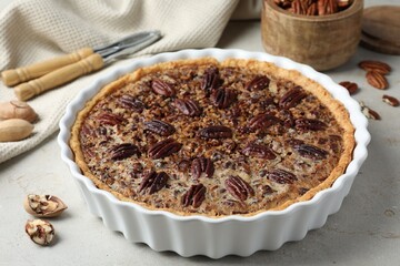 Wall Mural - Delicious pecan pie in baking dish and fresh nuts on gray textured table, closeup