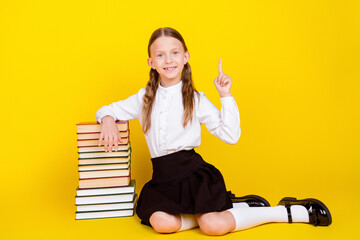 Poster - Full length photo of lovely small schoolgirl sit floor book pile point up empty space dressed uniform isolated on yellow color background