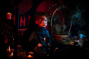 A little boy of two years old in a Viking costume against a background of candles and runes