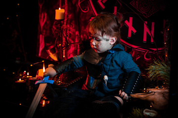 A little boy of two years old in a Viking costume against a background of candles and runes