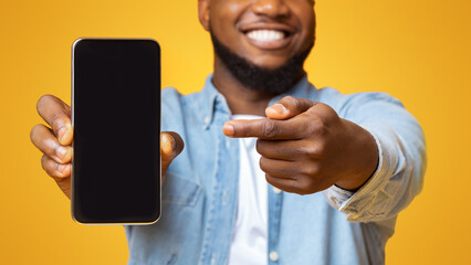 Check this app. Cheerful afro guy holding and pointing at smartphone with black screen, yellow background with free space