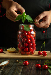 Sticker - A cook fills a jar with cherries and aromatic mint leaves before canning. Concept of canning delicious cherries.