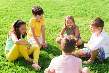 Group of kids sitting on field's green grass in summertime.