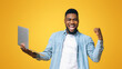 © Prostock-studio - Online lottery. Euphoric african man holding laptop and rejoicing success, shouting and raising clenched fist on yellow studio background