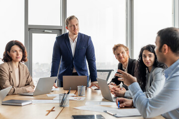 Aufkleber - A group of business professionals are gathered around a large wooden table in a modern office space. The men and women are engaged in a meeting, discussing ideas and strategies