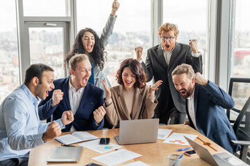 Aufkleber - A diverse group of business professionals gather around a laptop in a modern office setting, all cheering and raising their fists in celebration. They wearing business attire and appear to be thrilled