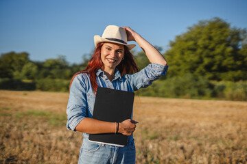 Portrait of young woman farmer stand in the field with clipboard