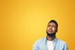 © Prostock-studio - Portrait of suspicious black guy looking upwards at copy space on yellow background.