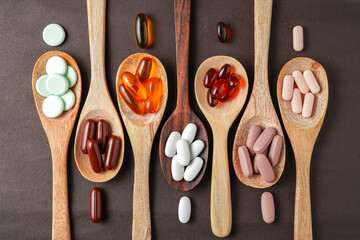 Wall Mural - wooden spoon with medical capsule pills, Dietary supplements vitamin on black background