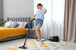 © New Africa - Young woman with headphones having fun while vacuuming carpet in bedroom