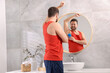 © New Africa - Smiling man applying solid deodorant near mirror at home