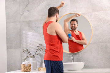 Wall Mural - Smiling man applying solid deodorant near mirror at home