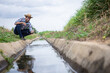 © kamonrat - Farmer Inspecting Water Flow in Irrigation Canal, Monitoring Agricultural Water Management and Sustainability in Crop Production